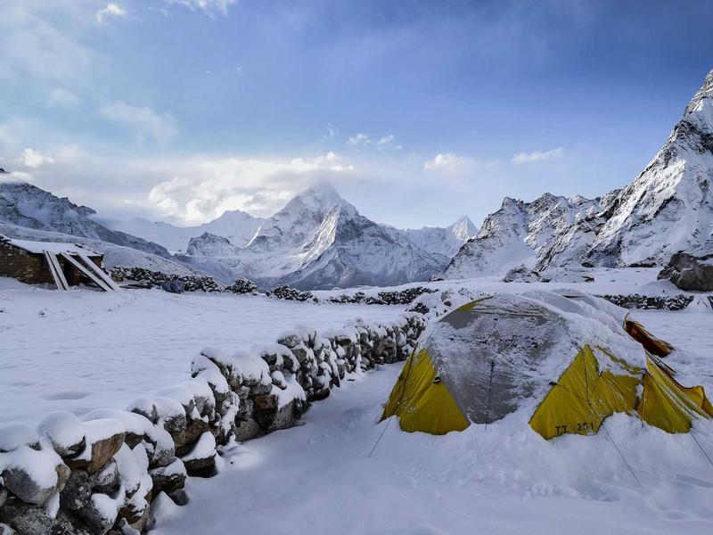 A yellow tent on snow-covered ground below a Himalayan peak