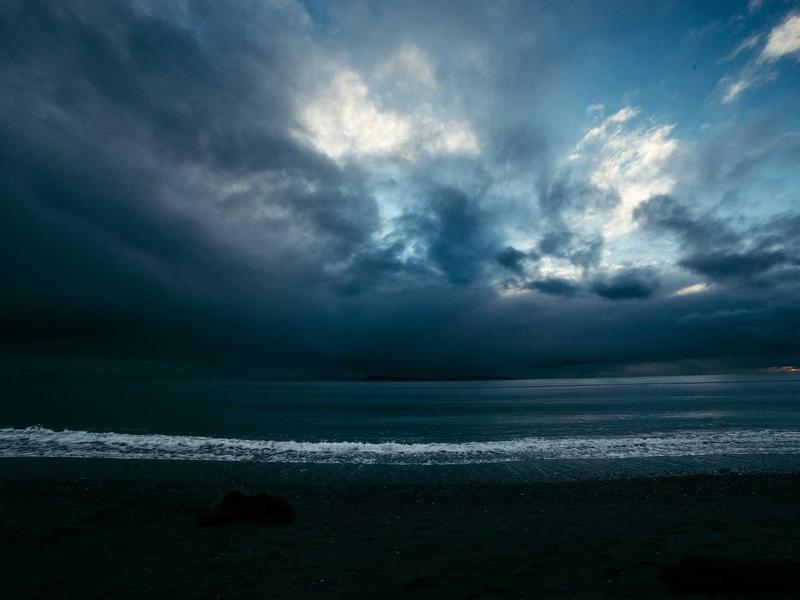 Heavy storm clouds breaking over a dark shoreline at dusk