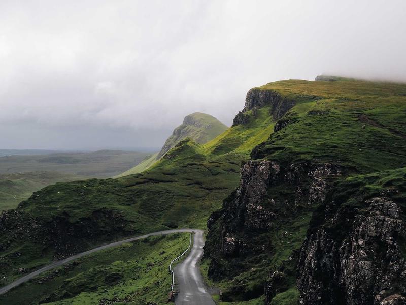 A single-track road curving along a steep green escarpment under low cloud