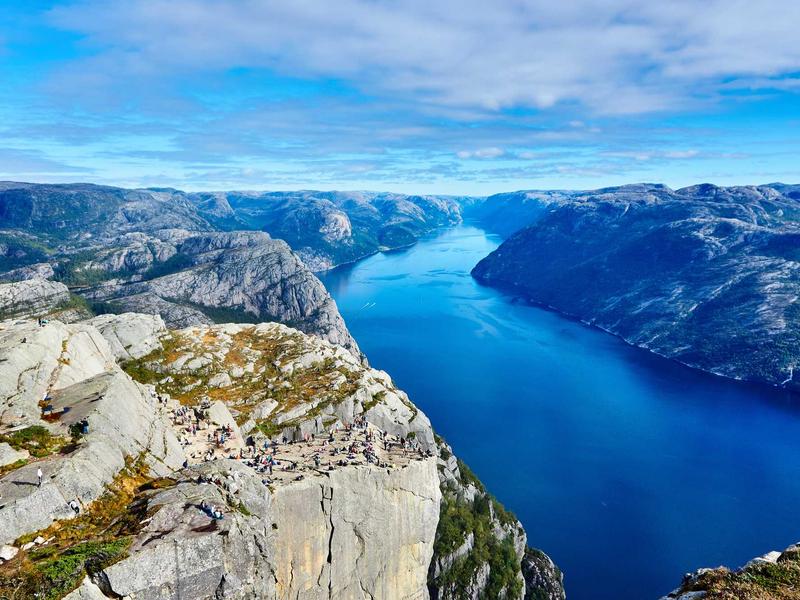 Walkers on a flat clifftop high above a deep blue fjord